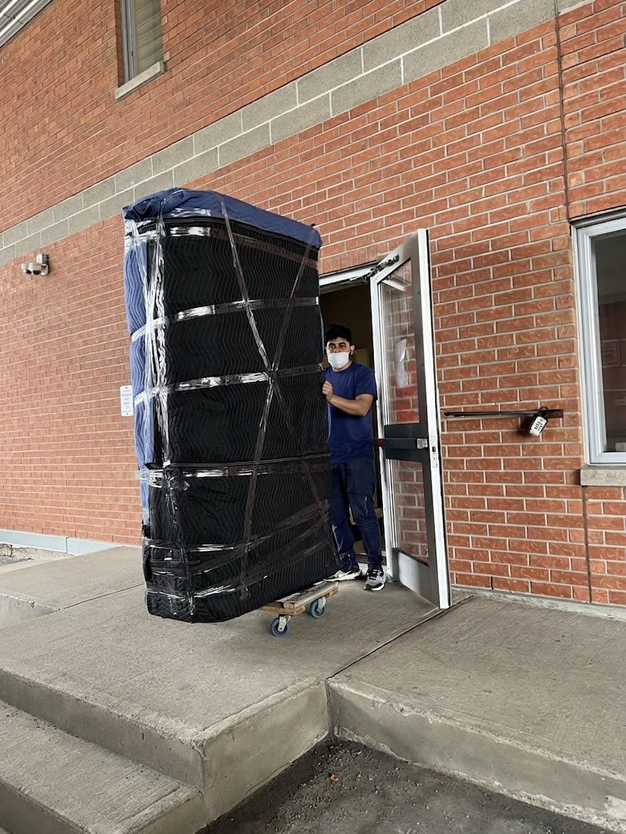 Grand meuble emballé et sanglé sur un chariot, franchissant la porte d'un immeuble