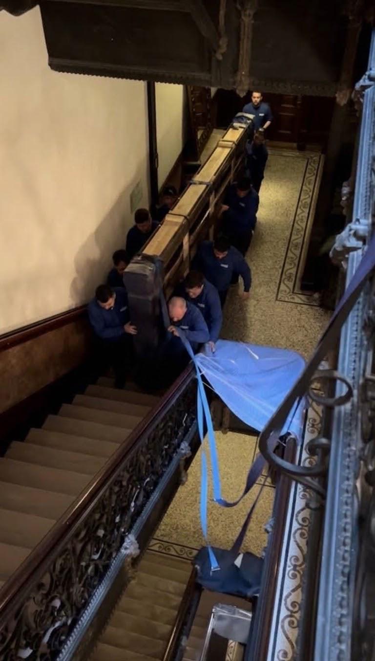 Équipe de déménageurs descendant un gros meuble emballé dans un escalier