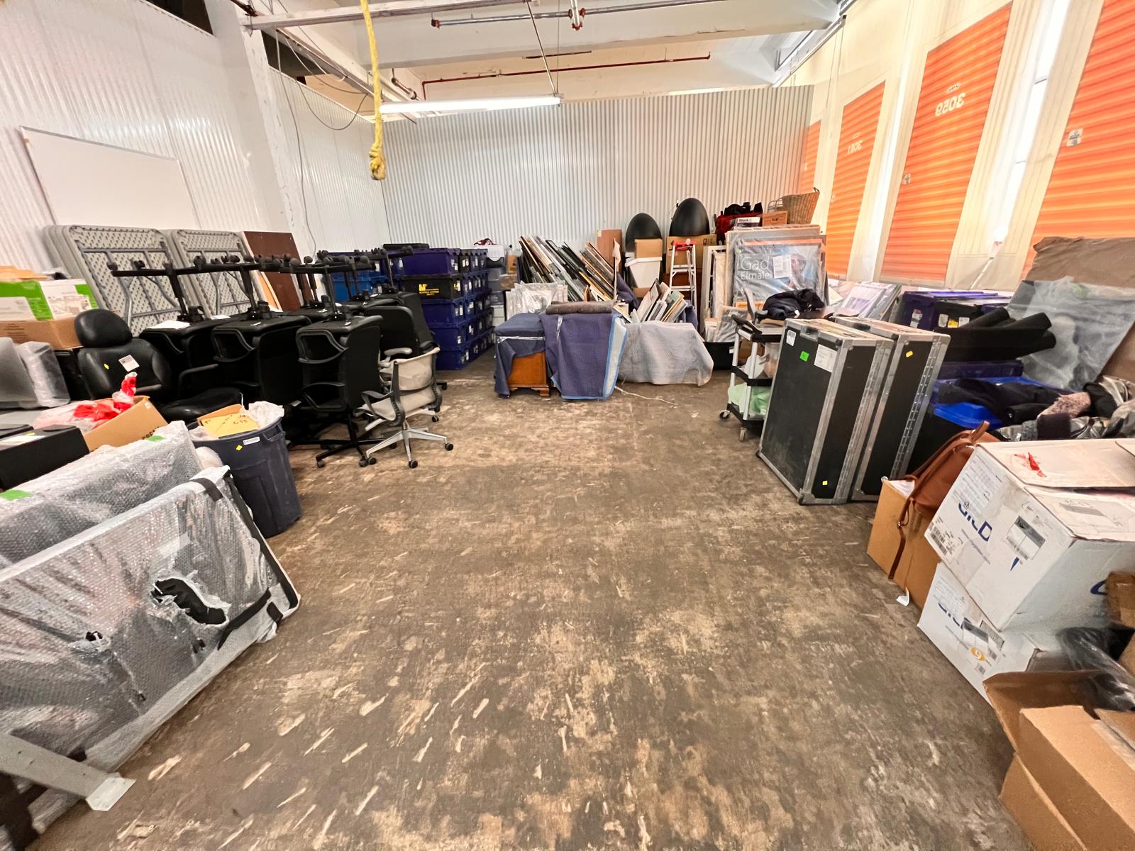 Entrepôt contenant le mobilier complet d'un bureau : chaises, tables pliantes, bacs et panneaux, rangés par catégorie