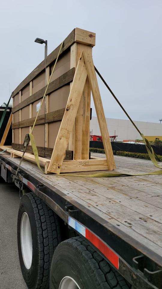 Grande pièce encaissée dans une ossature de bois sur mesure et sanglée sur une remorque plateau
