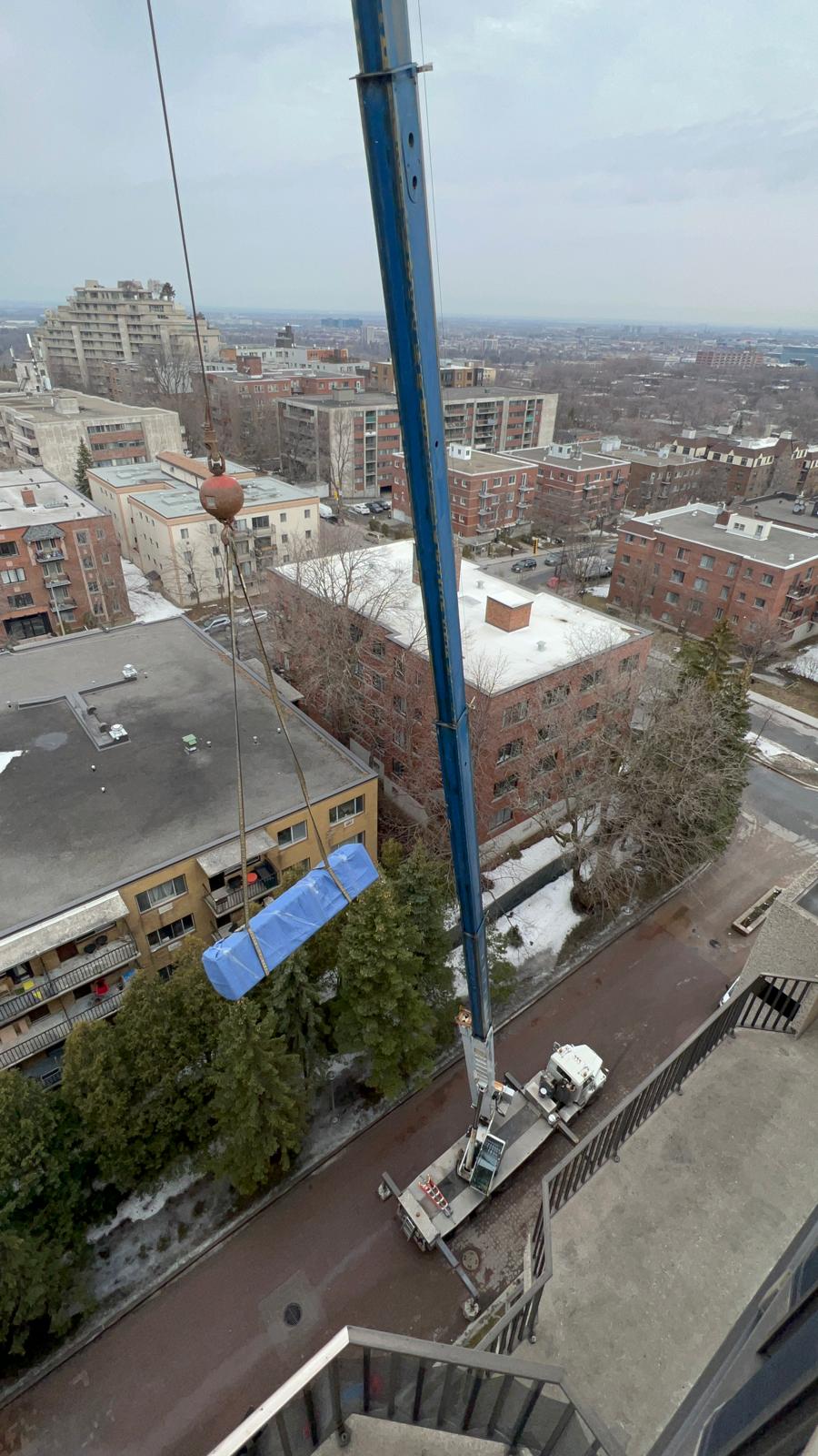Grue mobile hissant une pièce emballée le long d'une tour d'habitation, vue depuis un étage élevé