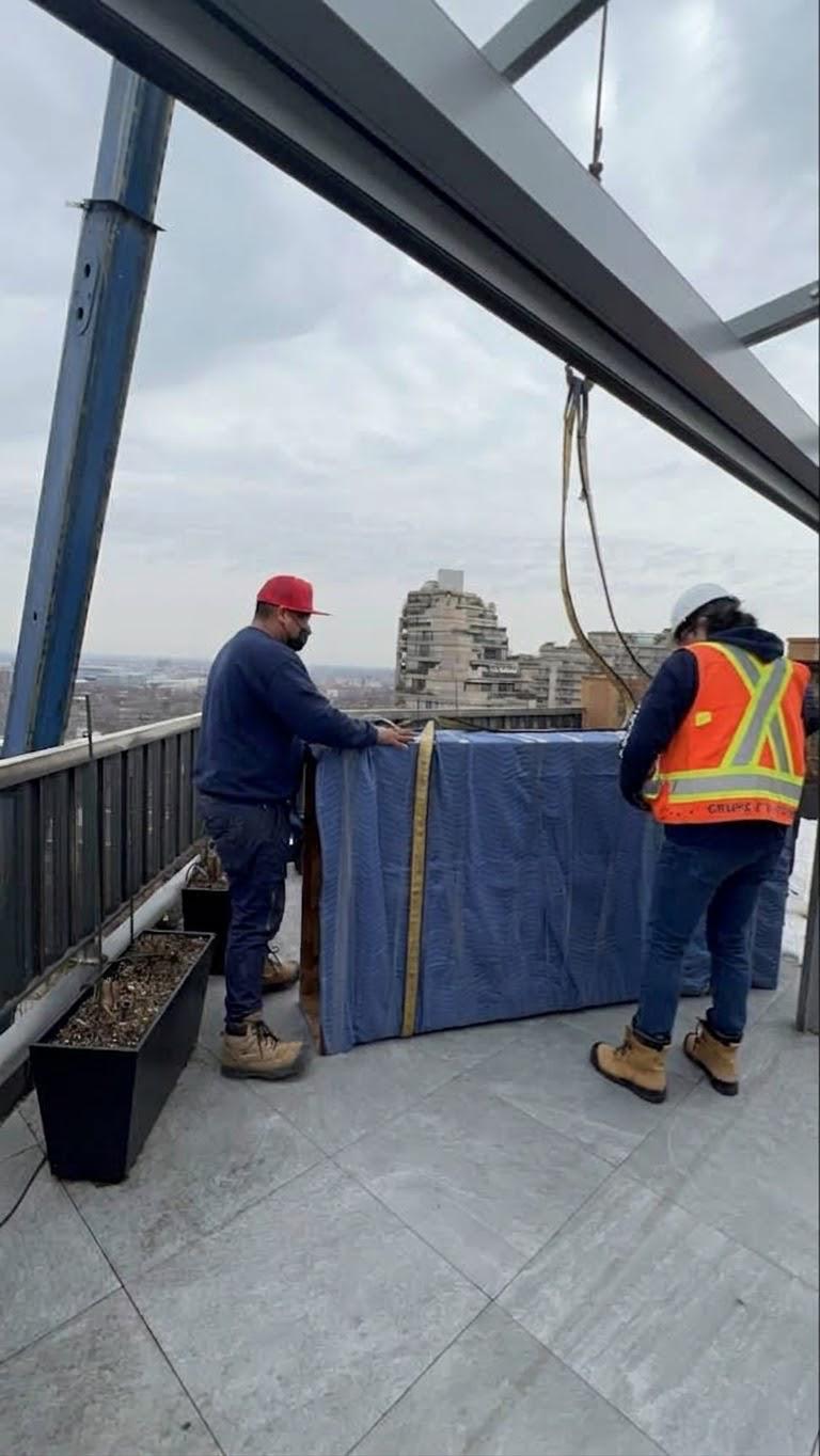 Deux déménageurs réceptionnant sur une terrasse en hauteur la pièce emballée encore accrochée à l'élingue