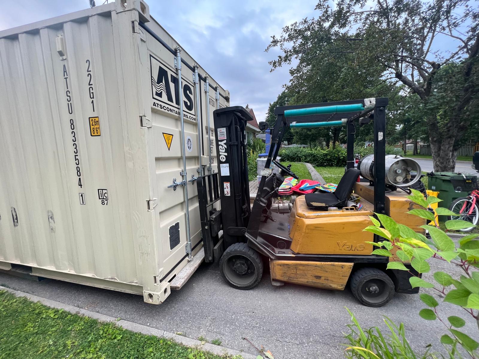 Conteneur maritime de 20 pieds livré dans une entrée résidentielle, chargé à l'aide d'un chariot élévateur