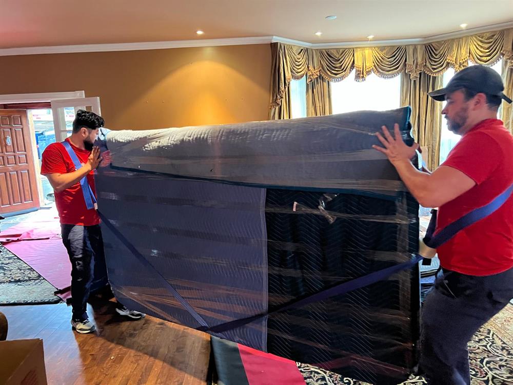 Two movers wrapping a large armoire in stretch film