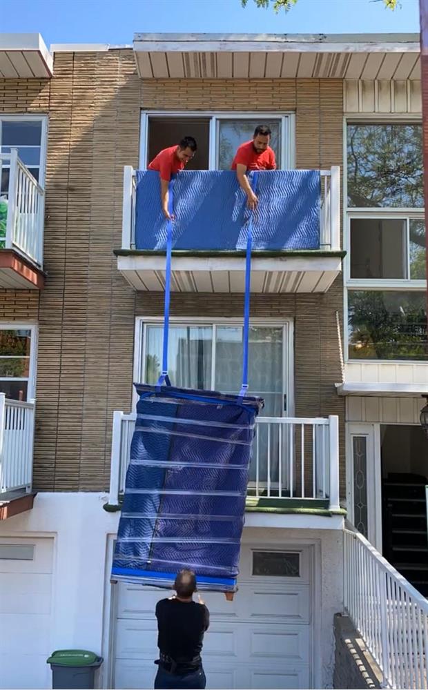 Deux déménageurs descendant un meuble emballé par le balcon avec des sangles