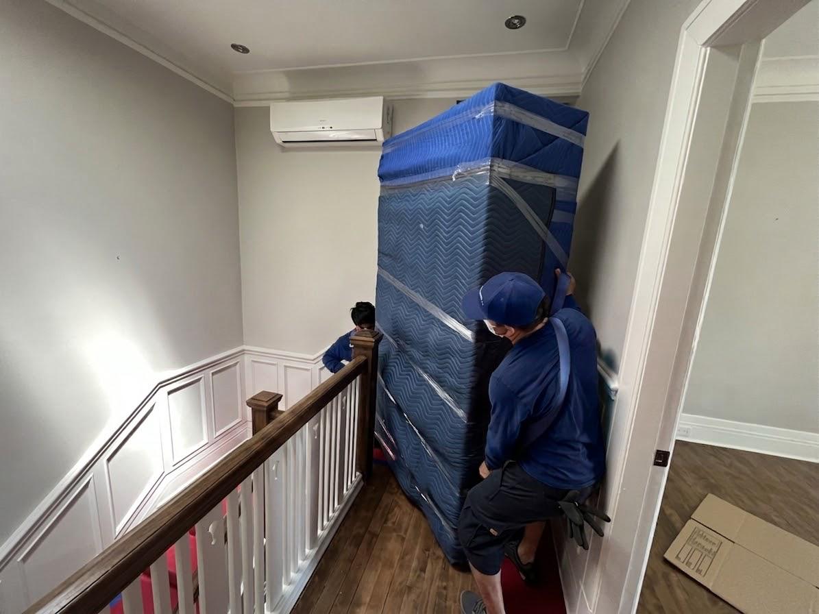 Deux déménageurs descendant un gros électroménager emballé dans un escalier intérieur