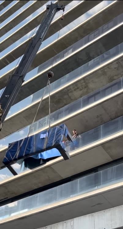 Meuble emballé hissé par grue jusqu'au balcon d'un étage supérieur
