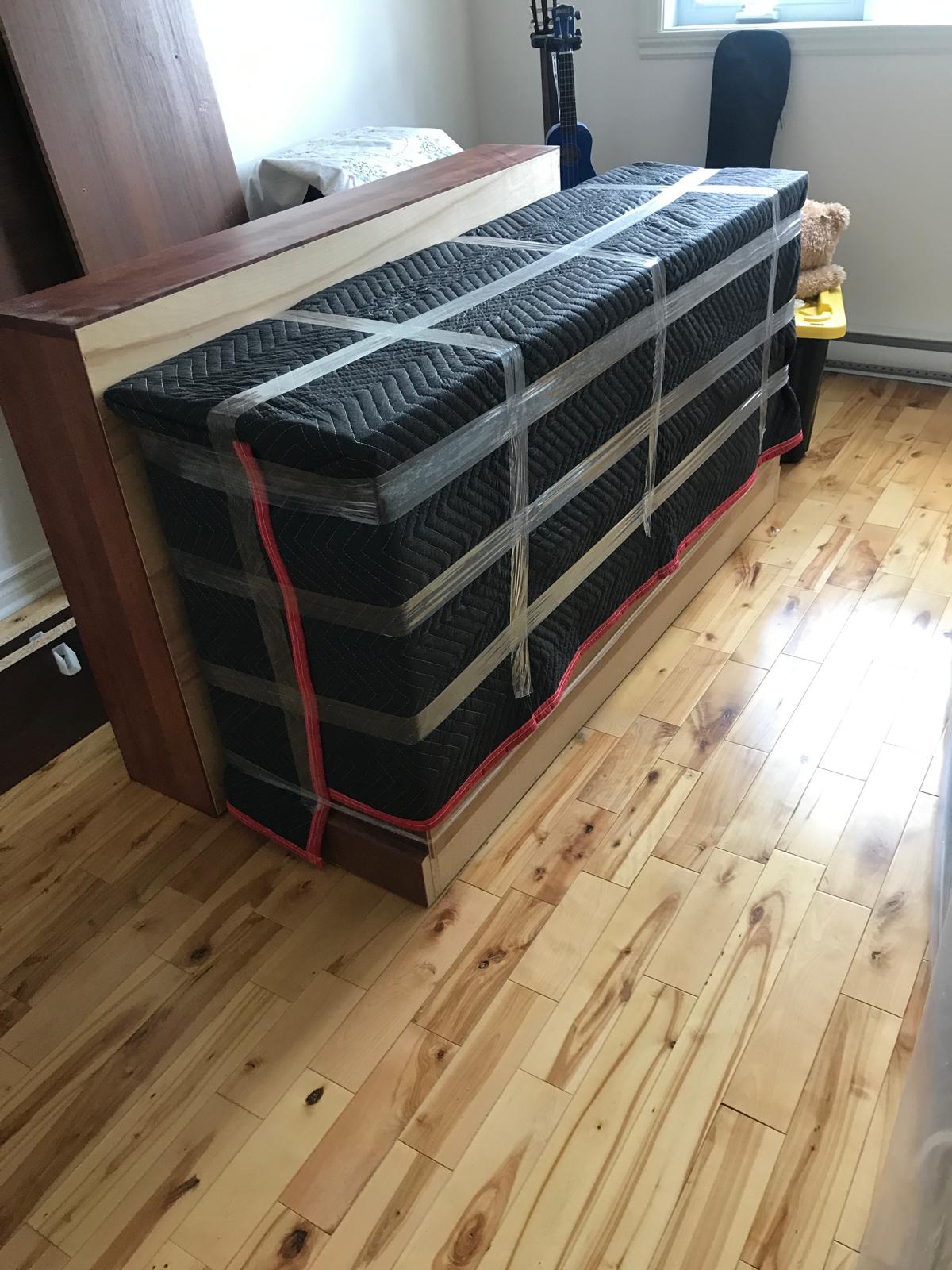 Sommier et matelas emballés et sanglés sur un plancher de bois