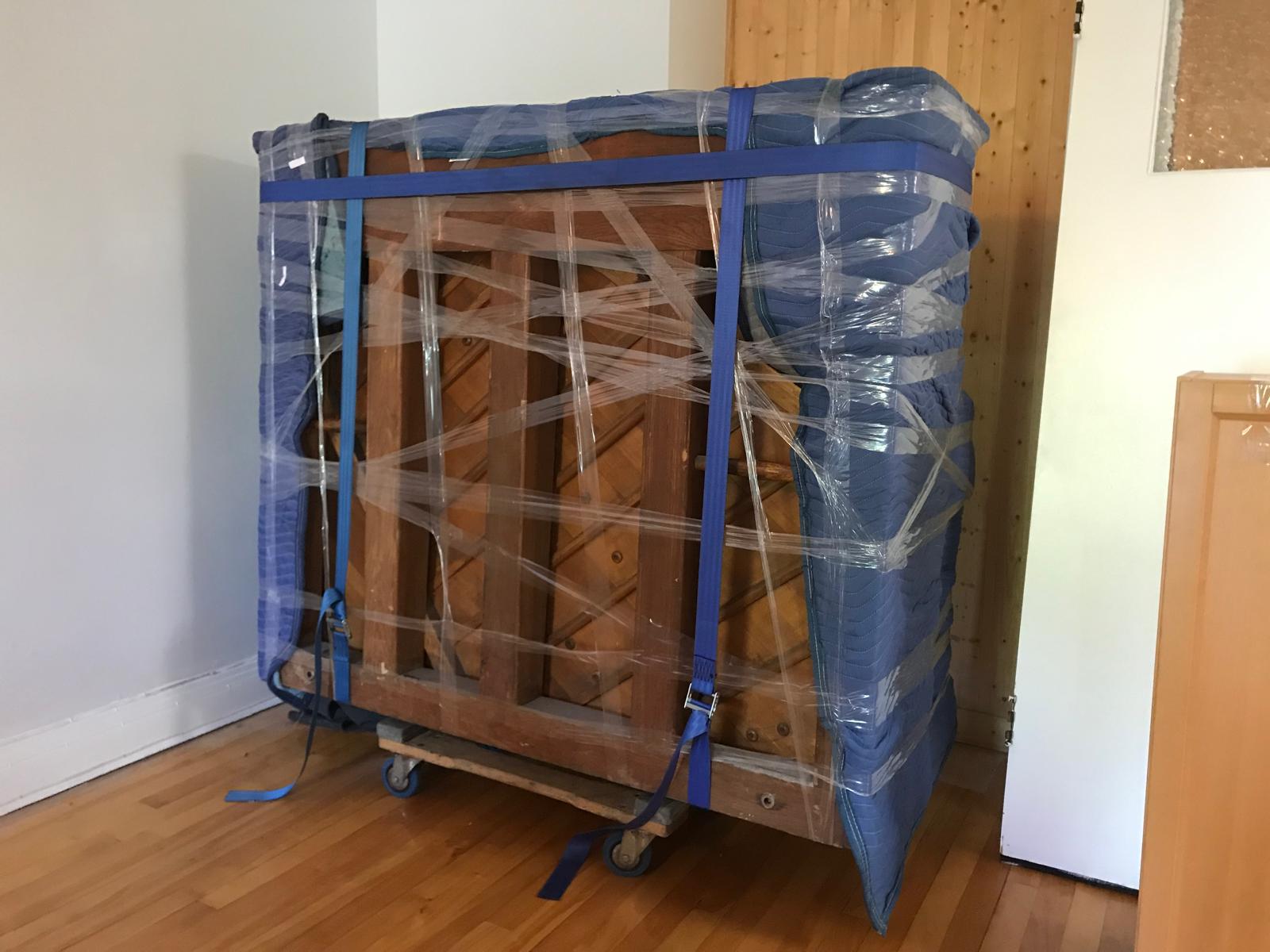 Piano emballé de pellicule et sanglé, calé sur un chariot dans une pièce
