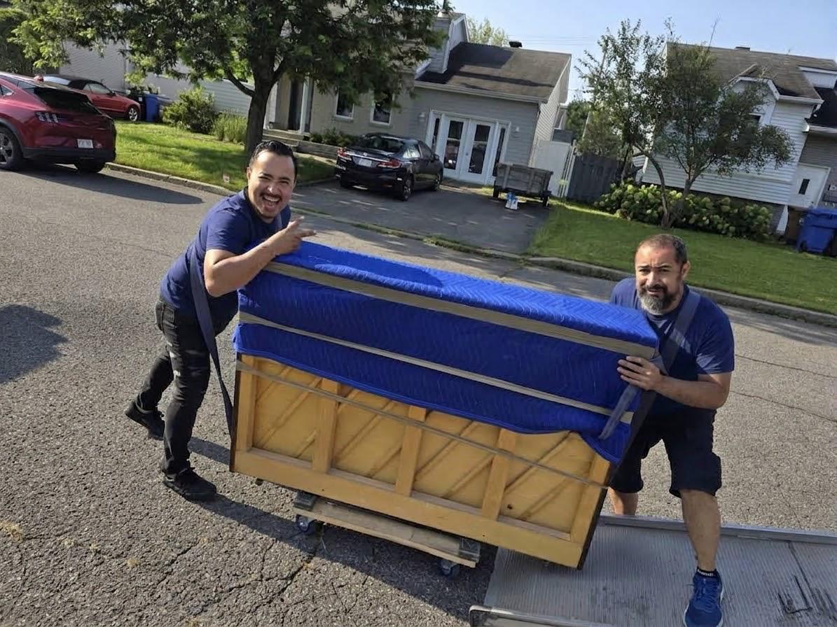 Deux déménageurs sortant un piano à queue emballé sur la planche, dans la rue