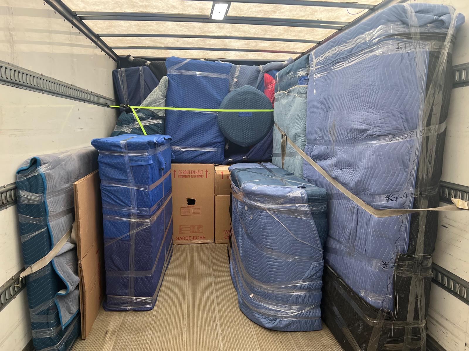 Intérieur d'un camion de déménagement chargé : meubles emballés dans des couvertures, sanglés par sections, boîtes garde-robe